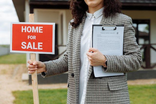 Woman holding a home for sale sign.