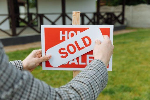 A person putting a sold sign over a for sale sign.